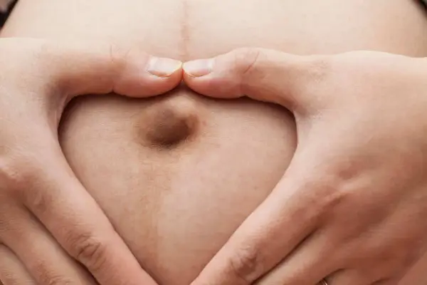 Mani a cuore circondano un ombelico in gravidanza, simbolo di amore e attesa.